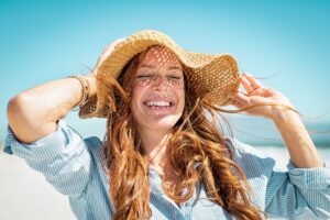 Woman with red hair wearing straw hat at the beach smiling