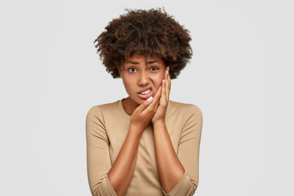 Woman in brown sweater pressing hands to her face in pain